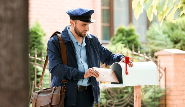 Handsome young postman putting letter in mail box outdoors