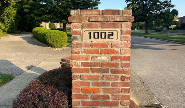 number 1002 on a concrete brick on a red brick mailbox with summer sunshine highlighting it